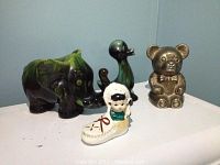 Full view of all five figurines including ceramic elephant, ceramic Eskimo boy in shoe, ceramic duck, and metal and ceramic bear figurines.