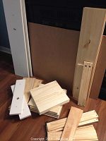 Assorted natural pine and painted wood boards and panels piled together on hardwood floor against wall.