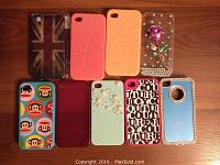 Nine iPhone 4 cases displayed on a wooden surface showing a variety of designs and colors.