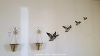 Photo of two gold-tone decorative bucket wall hangings on chains and multiple ceramic duck wall hangings mounted on wall.