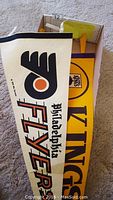 Photo showing both pennant flags, Philadelphia Flyers prominently displaying black and orange logo, and yellow Los Angeles Kings flag.