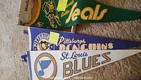 Three vintage NHL pennant flags for St. Louis Blues, Pittsburgh Penguins, California Golden Seals, arranged overlapping on carpet.
