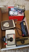 Box containing the Canon Sureshot 105u camera with original box, a Polaroid Swinger Model 20, Kodak Hawkeye Instamatic II, and another vintage camera.