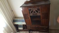 Wooden antique cupboard next to bookshelf with encyclopedias visible
