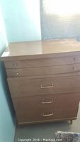 Front view of laminate wood dresser with four drawers and brass-colored metal handles