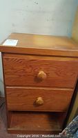 Front view of one wooden nightstand showing two drawers with wooden knobs and an open bottom shelf. Some surface scratches and wear are visible.