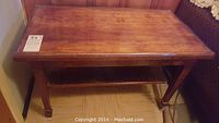 Wooden rectangular table positioned against wall, showing full top surface, legs, and lower shelf from the front view.