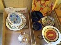 Assorted small blue glass bowls, a white plate with red and gold Japanese style design, and multiple small hand painted plates with floral and geometric patterns arranged together.