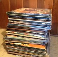 Stack of vinyl records on floor against wood panel wall