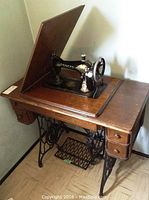 Singer sewing machine mounted on wooden table with drawers and treadle base