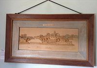 Full view of the framed balsa wood carving of village and river scene with wooden frame and fabric backing.