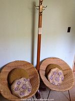 Full view of two round wicker chairs with throw pillows and the wooden coat tree behind them