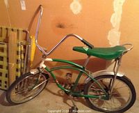 Side view of vintage green Savoy bicycle with banana seat, healthy chrome on handlebars and fenders, grass chair leaning in background