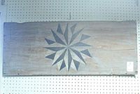 Lighted full view of large wooden panel with nautical star painted on rough wood surface hung on pegboard wall.