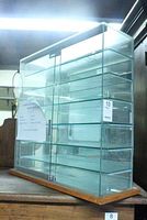 Front angled view showing the glass display case with six glass shelves, wooden base, and dual sliding doors with metal handles.