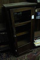Full front view of wooden cabinet with glass door closed, showing usage wear on top and sides.