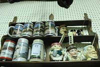 Photo showing 11 mugs on wooden shelf including steins with winter scenes and three character mugs detailing facial features and painted designs