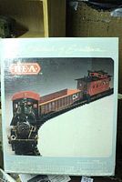 Photo of boxed model train featuring locomotive and caboose on track curve, showing front and side of packaging.