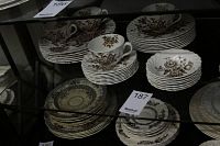 View of multiple plates, teacups, saucers and bowls arranged in display case, showing the brown floral pattern on cream ceramic.