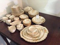 Full set of Limoges porcelain dinnerware with yellow daisy floral pattern and 22 KT gold trim displayed on table.