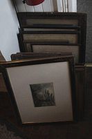 Photo showing a group of stacked framed vintage prints and several empty decorative wood frames behind them.