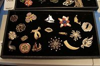 Tray containing an assortment of vintage brooches and pins in metal with various designs including flowers, ship, sailboat, crescent, and wings.