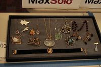 Full view of assortment of vintage costume jewelry including choker, necklaces, and pins arranged on black display background.