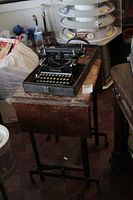 Black Corona folding typewriter in case sitting on top of rustic wood secretary desk with folding leaves and caster wheels.