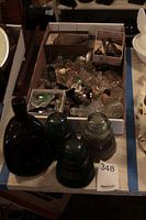 Photo of the box containing many glass bottle stoppers and three large glass insulators in front on a wooden plank.