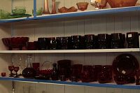 Three shelves of assorted ruby red glassware including plates, bowls, glasses, and pitchers arranged on white and blue shelves.