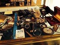 Photo of vintage pocket watches, wristwatches, eyeglasses and cases displayed on glass case.