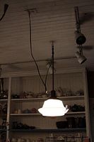 Full view of the antique school house hanging light illuminated, showing the white glass shade and brass pole hanging from the ceiling.