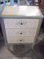 Front view of the small painted dresser showing its three drawers decorated with flower designs and single round knob handles.