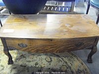 Full view of the vintage oak coffee table showing the curved front, wood grain surface, metal relief drawer pulls, and carved ornate feet.