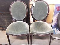 Pair of two upholstered chairs with dark wood frames, oval backs, and green velvet fabric seats and backs, showing wear and finish loss on wood surfaces.