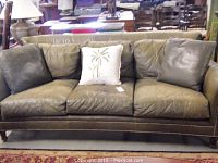 Full front view of green distressed leather sofa with three seat and back cushions and central throw pillow
