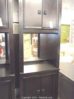 Front and left side view of tall dark wooden cabinet with closed upper and lower double doors, middle with open mirrored shelf.