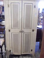 Front view of white wooden wardrobe with two paneled doors, brass tone hinges and ring pull handles, showing wear and paint loss.
