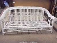 Front view of white painted wicker patio couch frame with open woven design.