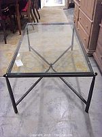 Full view from a low angle showing metal frame with diagonal stretchers and thick glass top.