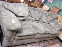 Full view of the green plush sofa showing three back cushions, three seat cushions, and rolled padded armrests.