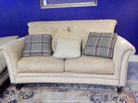 Front view of beige Ferguson Copeland loveseat with plaid and beige throw pillows, nail head trim, turned wooden legs.