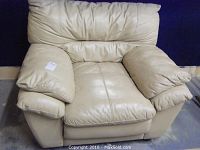 Front view of beige leather chair showing overall shape and wear on armrests