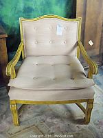 Front view of wooden armchair with beige button tufted upholstery and carved wooden frame.