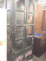 Full view of tall black curio cabinet with arched glass-paneled double doors, side panels, floral hand-painted design