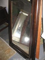 Full view of the beveled mirror showing its rectangular shape and wooden frame leaning against other furniture.