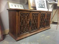 Full front and side view of the dresser showing the four carved wooden doors with metal backing and ornate metal latch hardware.