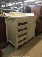 Side front view of white child changing table showing three glass front drawers and scalloped base trim