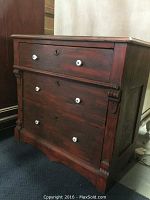 Red distressed wooden side table with three drawers, white porcelain handles, and keyholes, shown from the front.