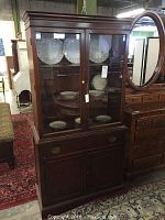Front view of Basset furniture china cabinet with glass-paneled doors showing interior shelves with plates and lower drawer and cabinet doors.